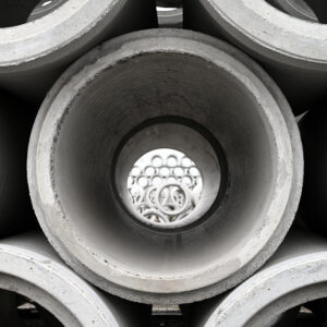 A close-up shot of stacked reinforced concrete pipe. A view through the center of the middle pipe shows more stacked pipes in the background.